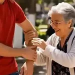 Persona adulta mayor recibe apoyo de un joven en espacio público