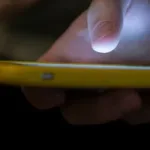 Persona usa un telefono inteligente junto a una computadora portatil