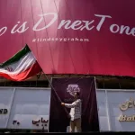 Hombre ondea bandera irani frente a cartel politico en Teheran