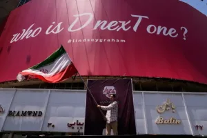 Hombre ondea bandera irani frente a cartel politico en Teheran